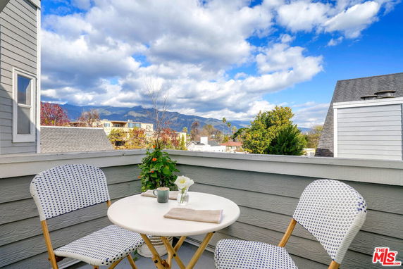 Outdoor balcony with table and chairs overlooking surrounding buildings and mountains.
