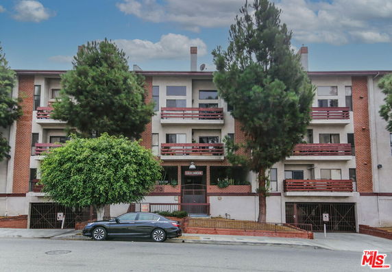 Front view of a multi-story apartment building with red brickwork and trees.