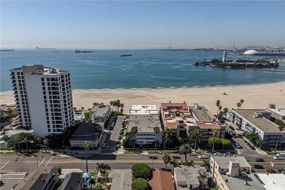 Aerial view of a coastal area with high-rise buildings and a beach, facing the ocean and distant shipping vessels.