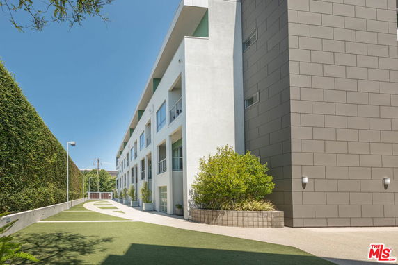 Side view of a modern multi-story building with large glass windows and a landscaped pathway.