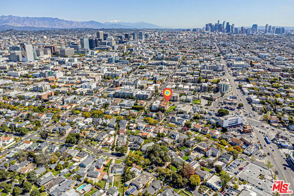 Aerial panoramic view of a large city with numerous buildings, roads, and a distant skyline.