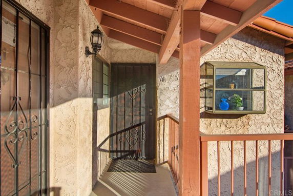 Front entryway of a house with textured walls, decorative wrought iron door, and covered porch.