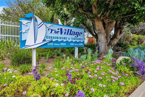 Sign for 'The Village Condominiums & Townhomes' with surrounding flowers and trees