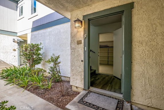 Front entrance view of a building with an open door leading inside, surrounded by plants and shrubs.