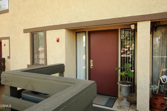 Front view of an apartment entrance with a wooden railing and plants.