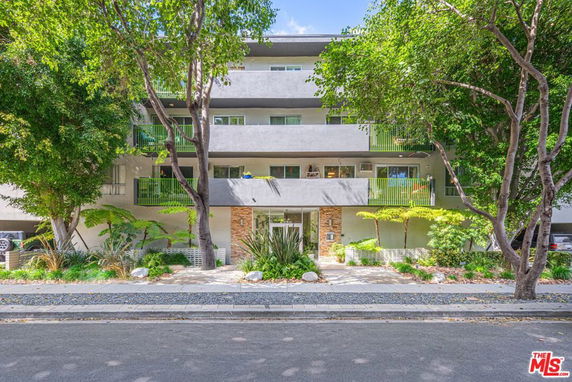 Front view of a multi-story residential building with balconies and surrounding trees.