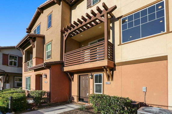 Front view of a multi-story house with a wooden balcony and tan exterior.