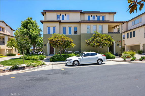 Front view of a three-story residential building with a central entrance and surrounding greenery.