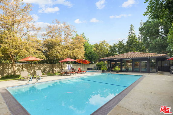 Outdoor swimming pool area with lounge chairs and umbrellas next to a building.