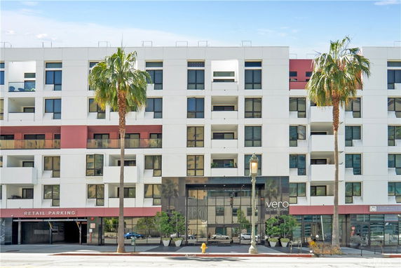 Front view of a multi-story building with modern architecture and palm trees in front.