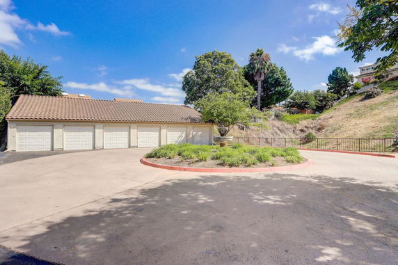 Outdoor parking area with multiple garage doors and surrounding vegetation.