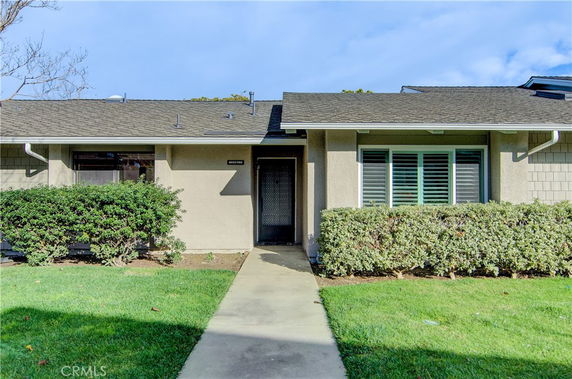 Front view of a single-story house with a walkway and bushes.