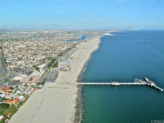Aerial panoramic view of a coastal city with a long beach and a pier extending into the ocean.