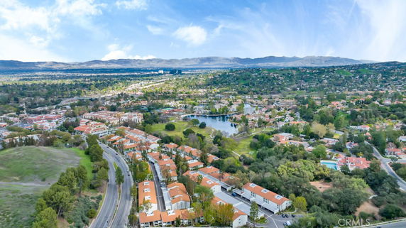 Aerial view of a residential area with buildings, roads, and greenery, set against a backdrop of distant mountains.