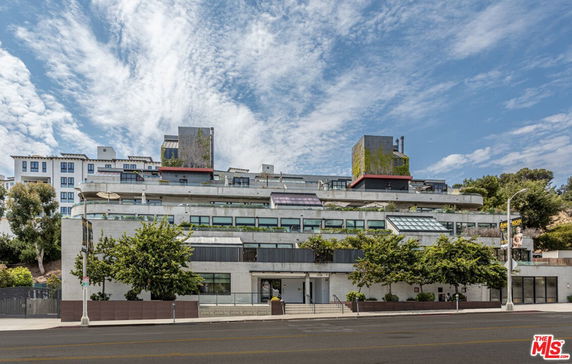 Front view of a multi-story modern building with rooftop vegetation.