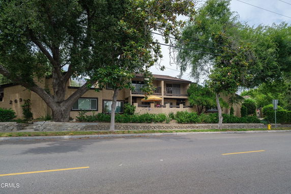 Front view of a two-story house with a balcony and surrounding greenery.