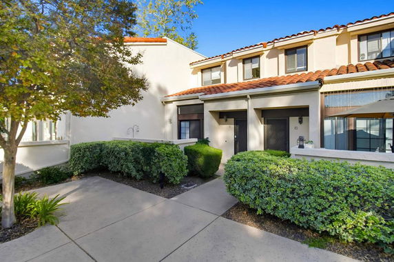 Front view of a two-story house with a tiled roof and small courtyard.