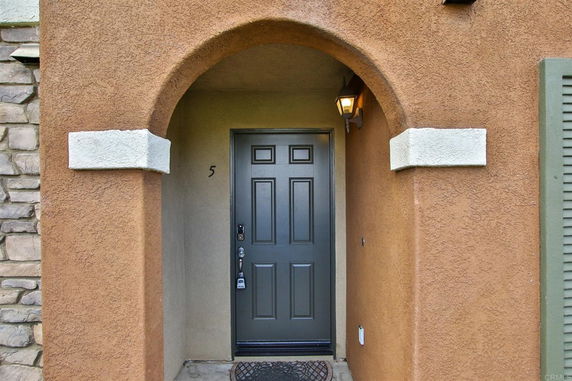 Front view of a house entrance with an arched doorway and brown stucco walls.