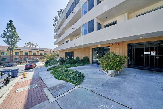 Front view of a multi-story building with a sidewalk entrance and greenery.