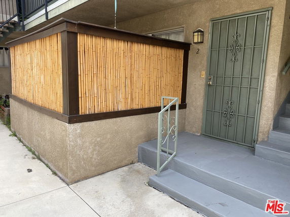 Front view of a building entrance with a bamboo fence and metal door.