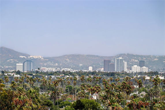 Wide view of a city skyline with tall buildings and mountains in the background.