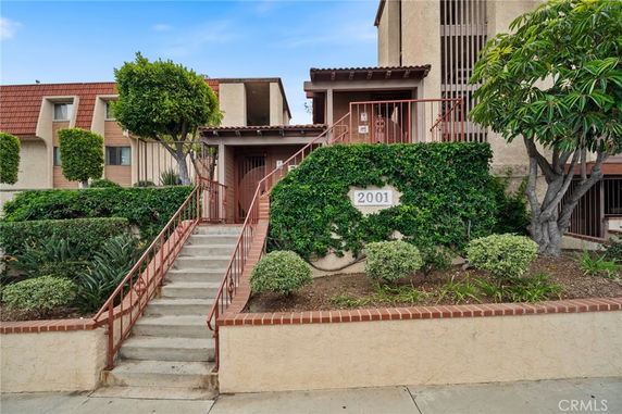 Front view of a multi-story building entrance with stairs and greenery.