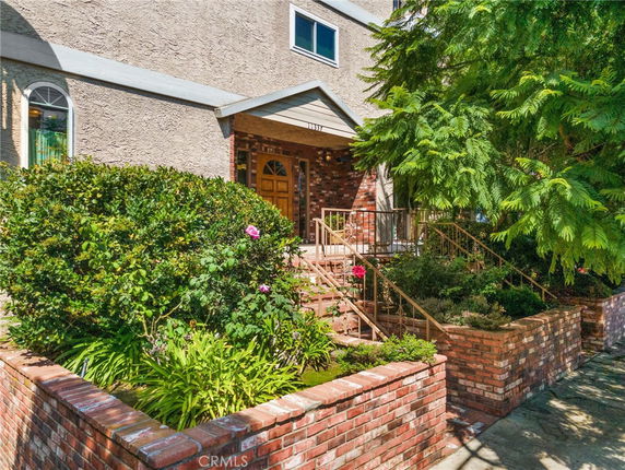 Front view of a house with brick and stucco exterior, featuring an entrance with stairs and garden.