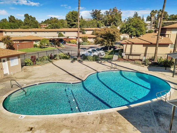 View of a kidney-shaped outdoor swimming pool with nearby buildings in a residential area.