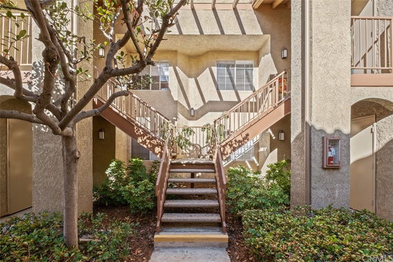 Front view of a building with external staircases and beige stucco walls.