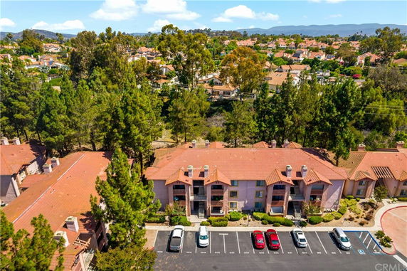 Aerial view of a residential area featuring multiple houses with red-tiled roofs and tall trees.