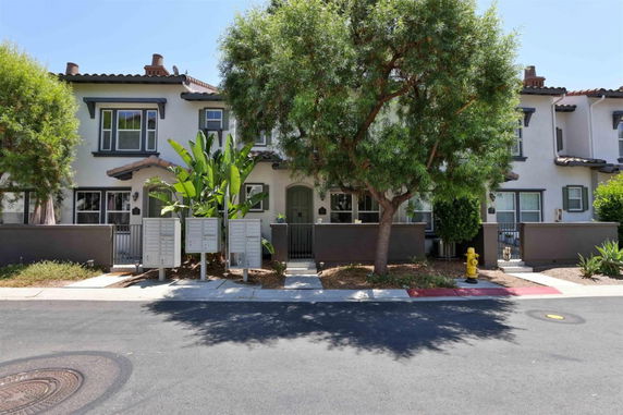 Front view of a two-story townhouse with a gated entrance and surrounding greenery.