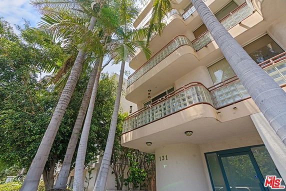 Front view of a multi-story building with glass block railings and palm trees nearby.