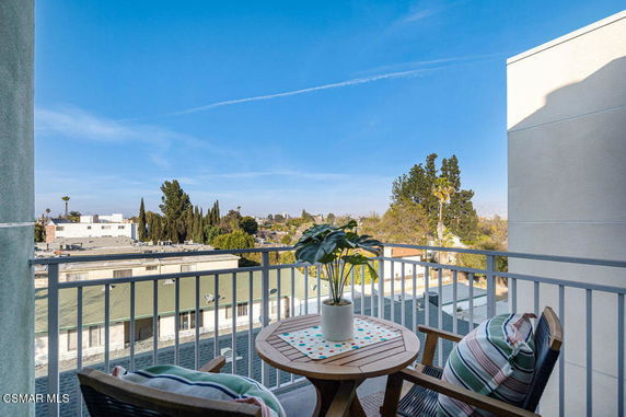 View from a balcony with chairs and a table, overlooking nearby buildings and trees.