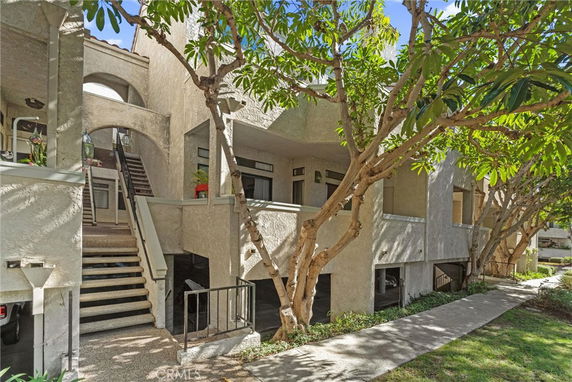 Front view of a multi-story residential apartment building with staircases and trees surrounding the area.