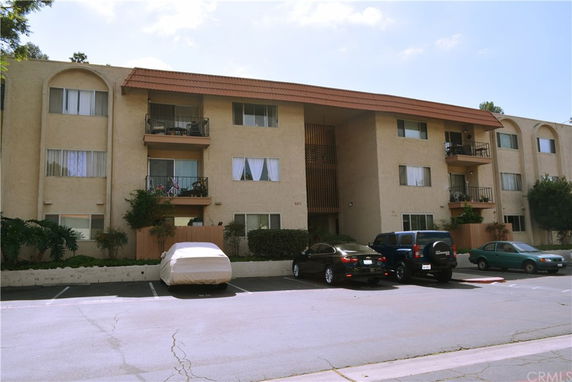 Front view of a three-story residential building with balconies and parking area.