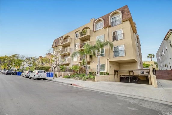 Front view of a multi-story apartment building with balconies and a parking garage entrance.