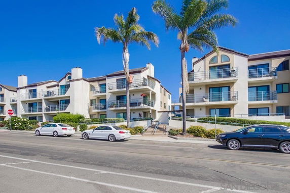 Front view of a multi-story apartment building with balconies and palm trees.
