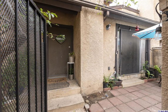 Front view of a small entryway with a welcome sign on the door and a patio area.
