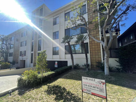 Front view of a multi-story residential building with large windows and a for sale sign in front.