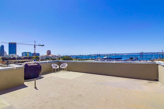 Rooftop with view of cityscape and waterfront, featuring a barbecue grill and chairs.