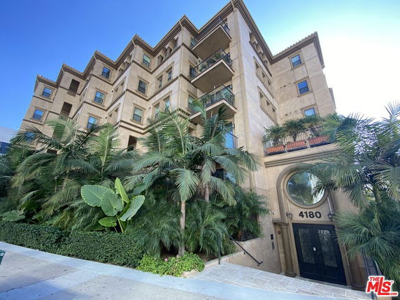 Front view of a multi-story building with balconies and lush greenery.