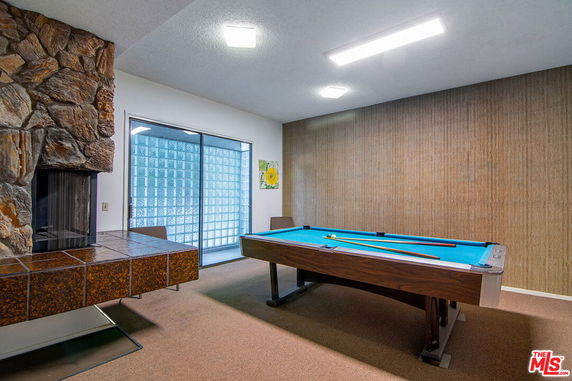 Indoor recreation room with a pool table and a stone fireplace.