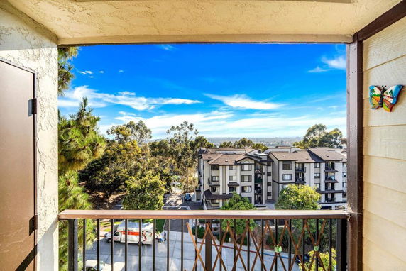 Panoramic view from a balcony showcasing a building complex and surrounding trees.