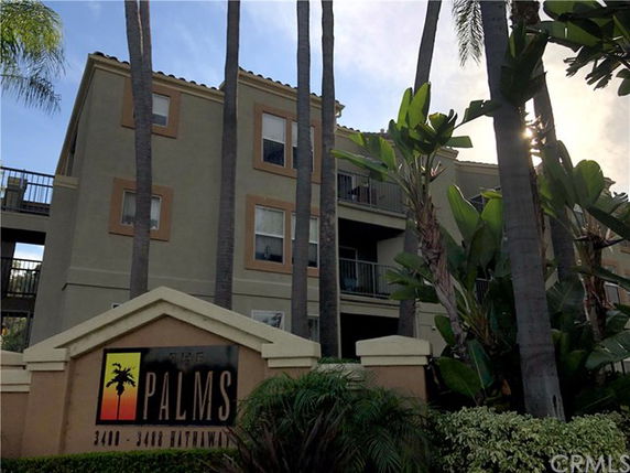 Front view of a multi-story apartment complex with palm trees and a sign labeled 'The Palms'.