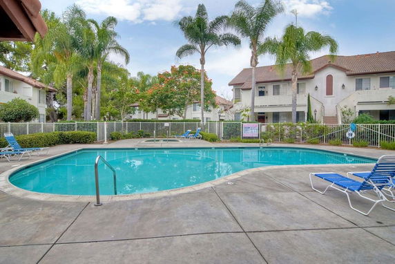 Outdoor swimming pool area with surrounding buildings and palm trees.
