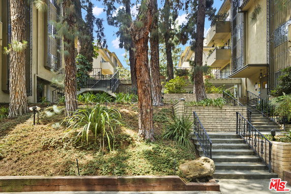 Front view of a multi-story building with stairs and vegetation.