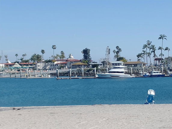 Coastal view with boats docked at a marina, palm trees, and a sandy beach in the foreground.