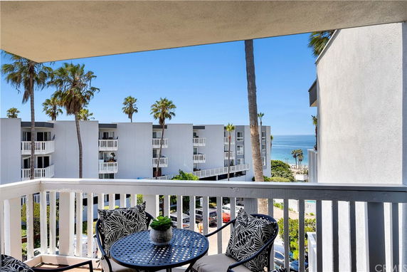 View from balcony showing buildings, palm trees, and ocean in the background.