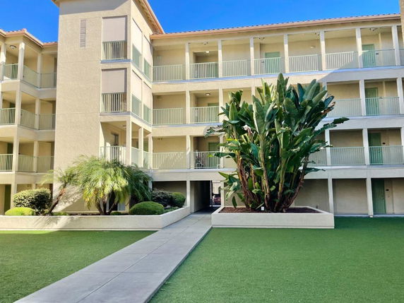 Front view of a multi-story building with balconies and a pathway leading to the entrance.