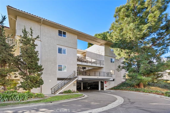 Front view of a multi-story apartment building with exterior staircases and covered parking.